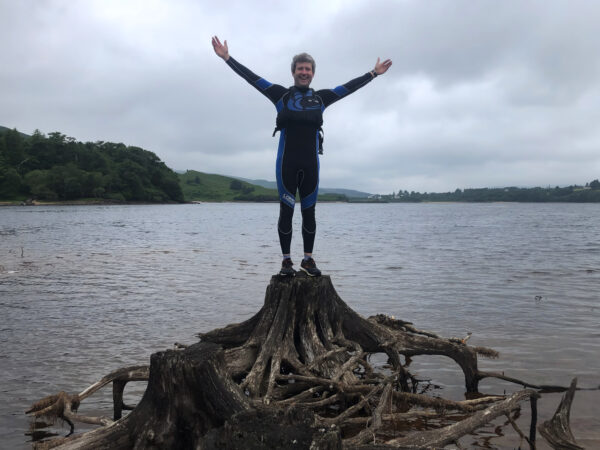 A man standing on a tree root in the middle of Dunlewey Lake