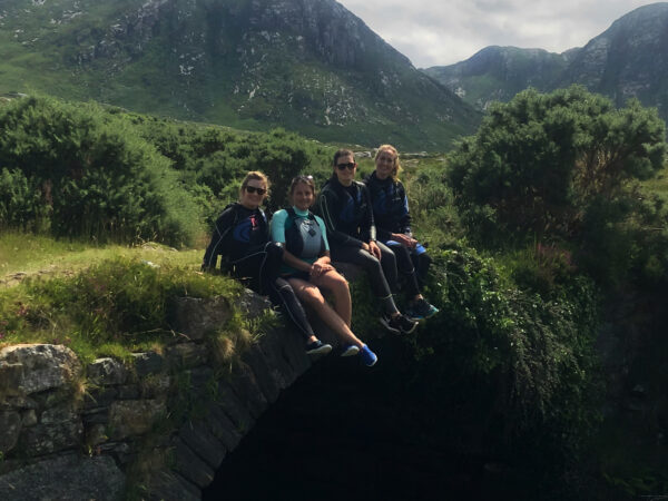 A group of friends sitting on a bridge with beautiful scenery and mountains in the background