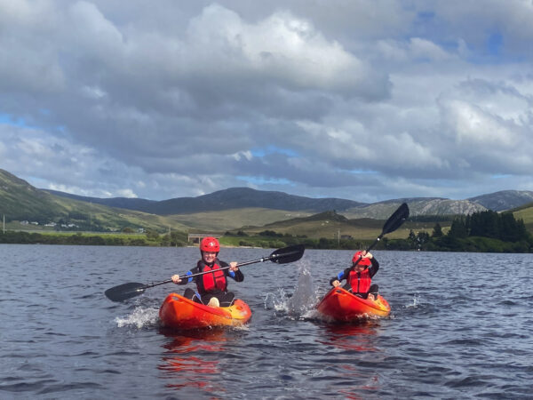 Two kids kayaking on Dunlewey Lake in the sunlight