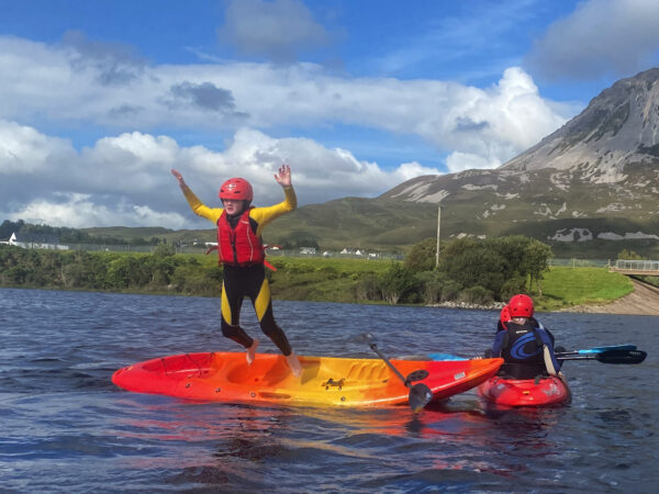 A boy jumps off a kayak while Kayaking on Dunlewey Lake