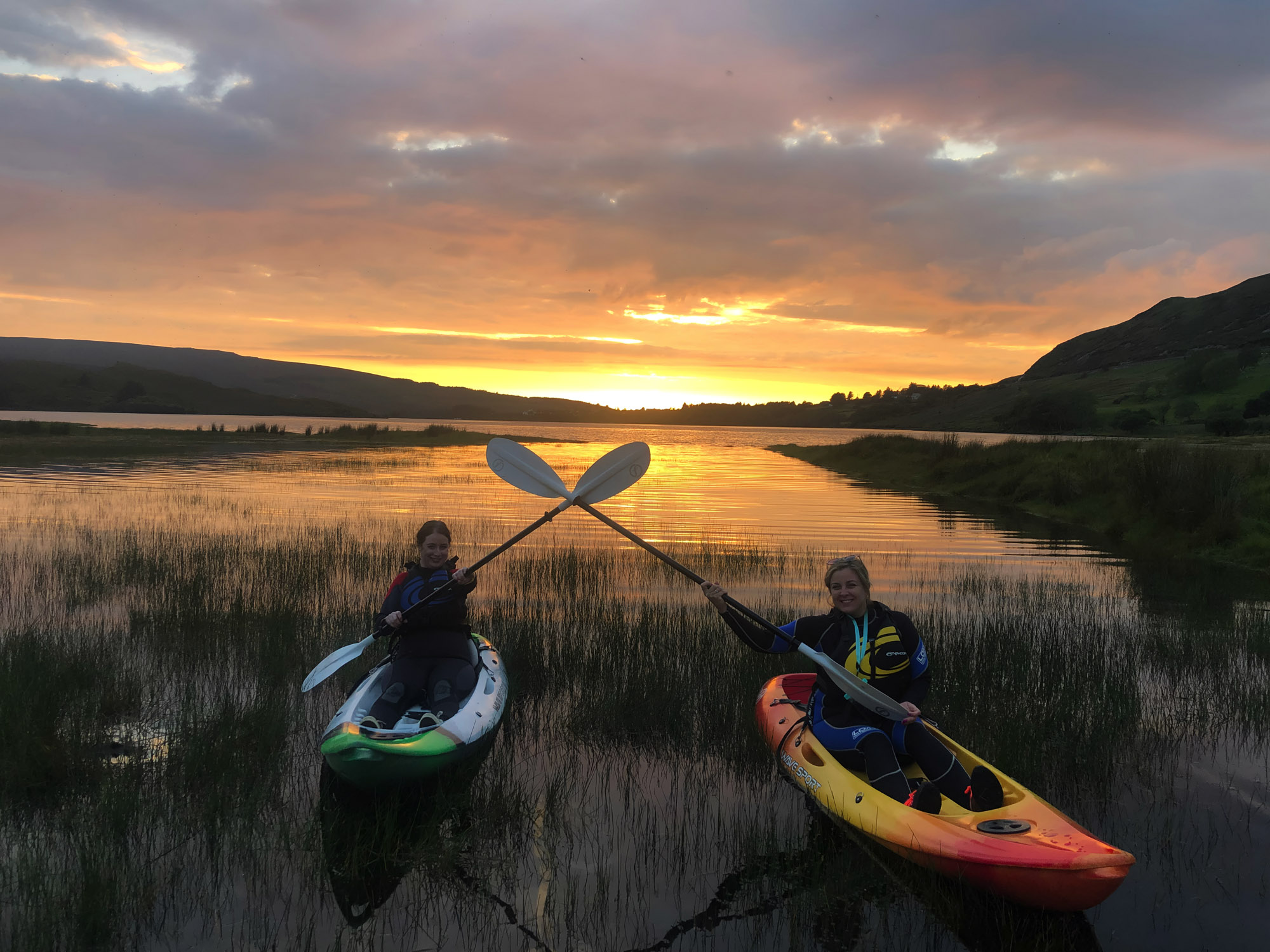 2 young women kayaking on Dunlewey Lake and crossing their paddles playfully