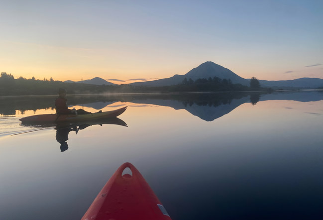 Kayaking at sunrise on Dunlewey Lake with a view of the lake like a mirror